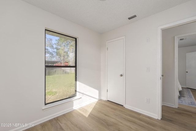 unfurnished room with a textured ceiling, wood finished floors, visible vents, and baseboards