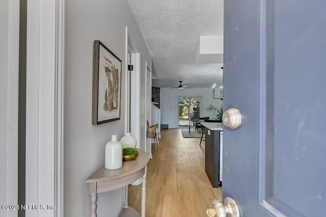 hall with a textured ceiling and light wood finished floors