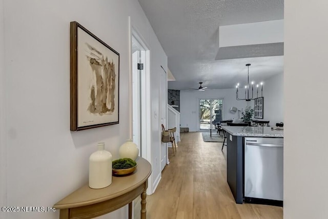 kitchen featuring light stone counters, stainless steel dishwasher, light wood-style floors, a textured ceiling, and ceiling fan with notable chandelier