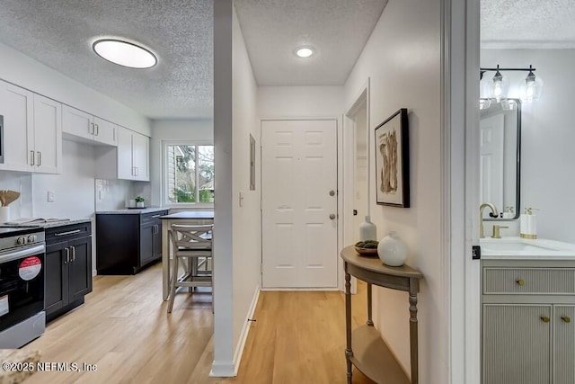 kitchen with light countertops, electric range, light wood-style floors, white cabinetry, and a sink