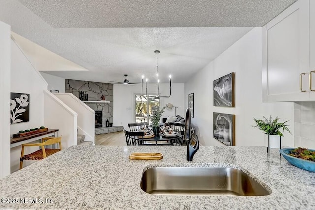 kitchen with white cabinets, a sink, a stone fireplace, a textured ceiling, and light stone countertops