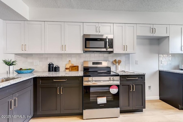 kitchen featuring a textured ceiling, appliances with stainless steel finishes, backsplash, and white cabinetry