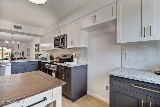 kitchen with stainless steel appliances, backsplash, visible vents, and white cabinetry