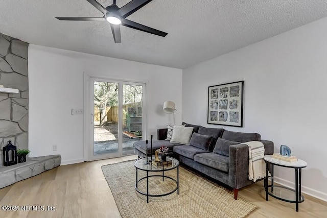 living room with a ceiling fan, a textured ceiling, baseboards, and wood finished floors