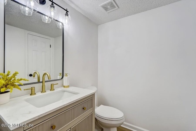 half bath with a textured ceiling, toilet, vanity, visible vents, and baseboards