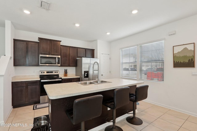 kitchen featuring stainless steel appliances, visible vents, dark brown cabinets, light countertops, and a kitchen bar