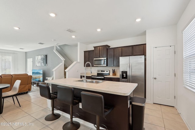 kitchen featuring light tile patterned flooring, a sink, dark brown cabinets, appliances with stainless steel finishes, and light countertops