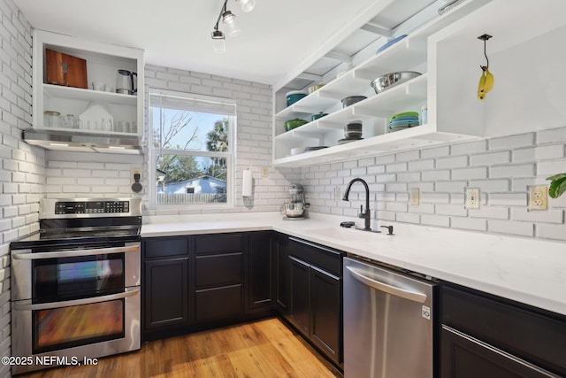 kitchen featuring open shelves, decorative backsplash, appliances with stainless steel finishes, and a sink