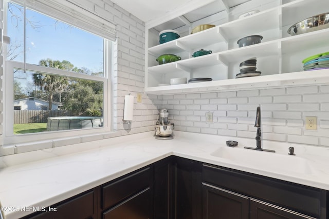 kitchen featuring light stone counters, backsplash, open shelves, and a sink