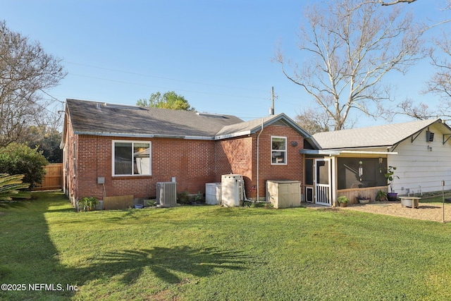 rear view of property featuring a yard, fence, brick siding, and a sunroom