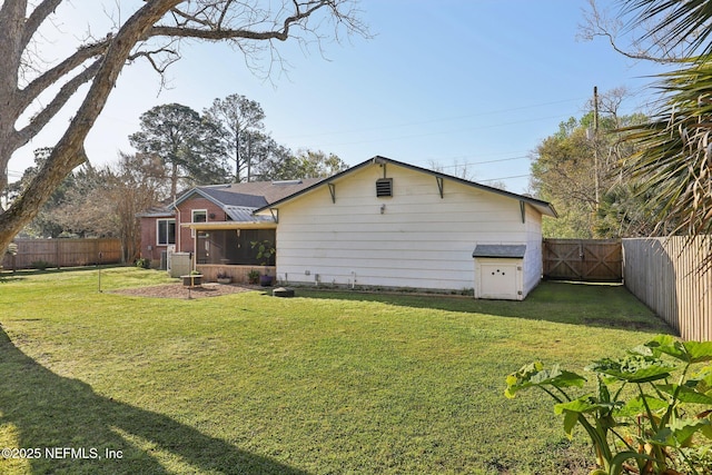 rear view of property featuring a gate, a fenced backyard, a lawn, and a sunroom