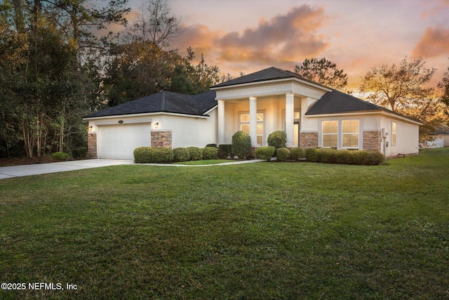 neoclassical / greek revival house with driveway, a garage, stone siding, a front yard, and stucco siding