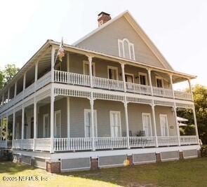 view of front of property with a front yard, covered porch, a chimney, and a balcony