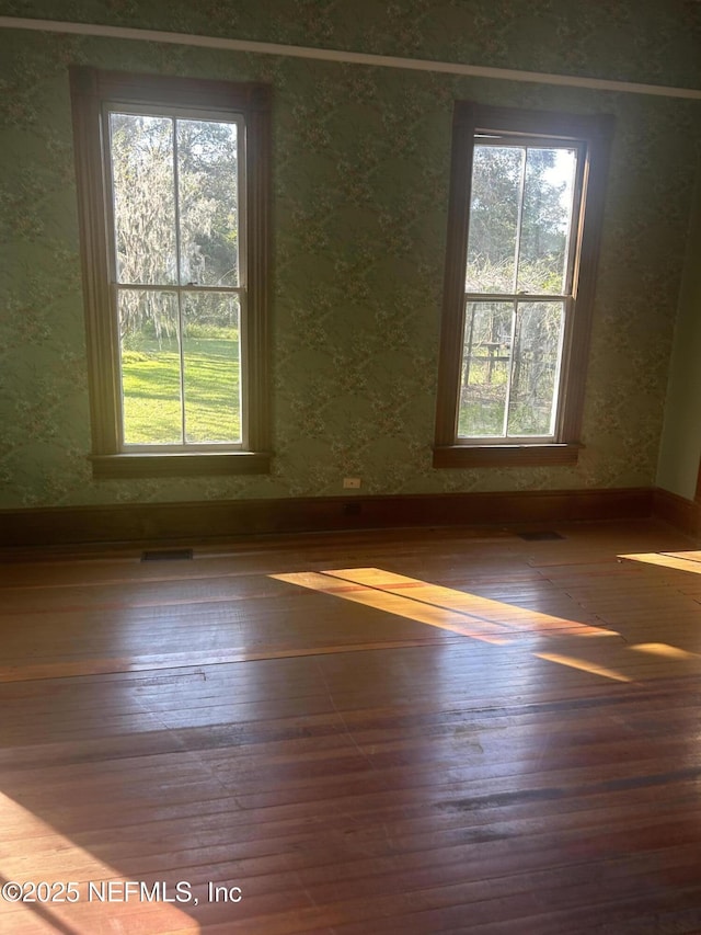 empty room with wood-type flooring, visible vents, and baseboards