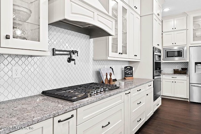 kitchen featuring stainless steel appliances, premium range hood, light stone counters, and white cabinetry