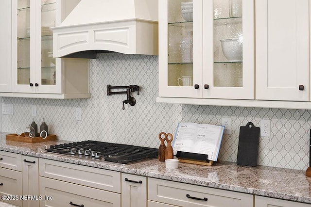 kitchen featuring light stone counters, white cabinetry, stainless steel gas cooktop, and premium range hood