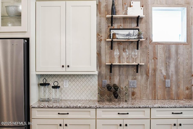 kitchen with light stone counters, freestanding refrigerator, white cabinetry, open shelves, and backsplash