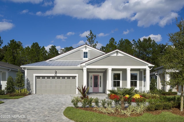 view of front of house with decorative driveway, a porch, an attached garage, a standing seam roof, and metal roof