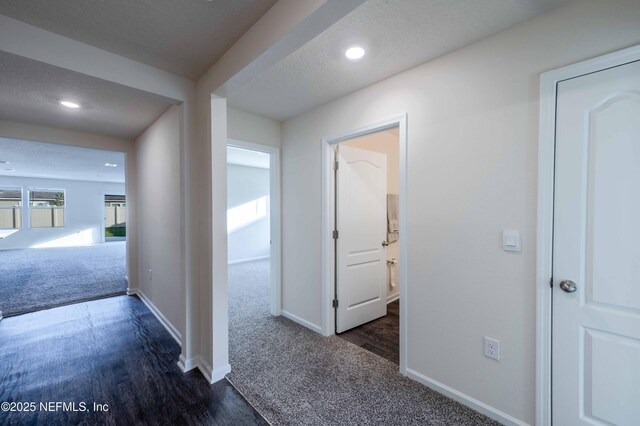 corridor featuring carpet floors, baseboards, a textured ceiling, and wood finished floors