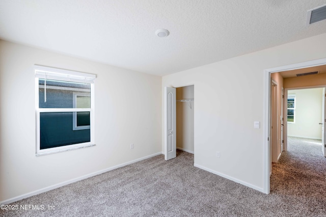 unfurnished bedroom with a textured ceiling, carpet, visible vents, and baseboards