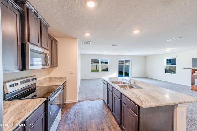 kitchen featuring visible vents, appliances with stainless steel finishes, open floor plan, a kitchen island with sink, and a sink