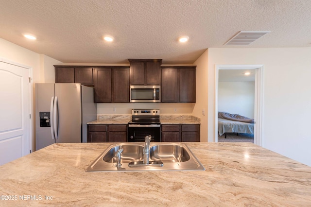 kitchen with a sink, visible vents, light countertops, appliances with stainless steel finishes, and dark brown cabinets