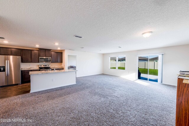 kitchen with a kitchen island with sink, stainless steel appliances, open floor plan, dark brown cabinets, and light countertops