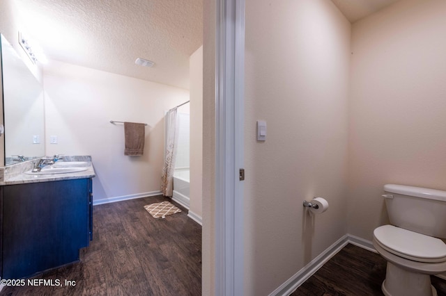 full bathroom with toilet, vanity, a textured ceiling, wood finished floors, and baseboards