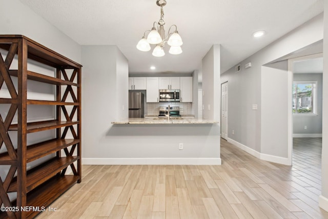 kitchen with light wood finished floors, appliances with stainless steel finishes, backsplash, and decorative light fixtures