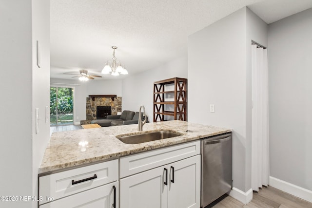 kitchen with a fireplace, white cabinets, a sink, light stone countertops, and dishwasher