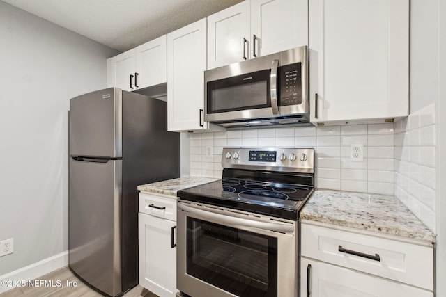 kitchen with light wood finished floors, appliances with stainless steel finishes, light stone counters, white cabinetry, and backsplash