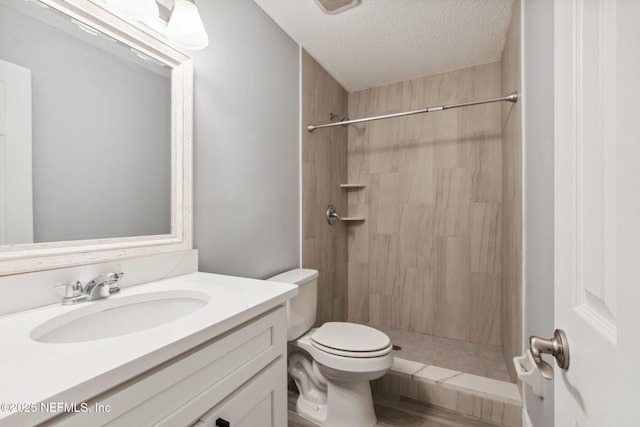 bathroom featuring toilet, a tile shower, a textured ceiling, and vanity