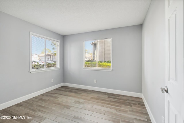 unfurnished room with light wood-style floors, plenty of natural light, baseboards, and a textured ceiling