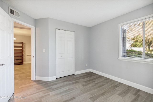 unfurnished bedroom featuring light wood-type flooring, baseboards, visible vents, and a closet