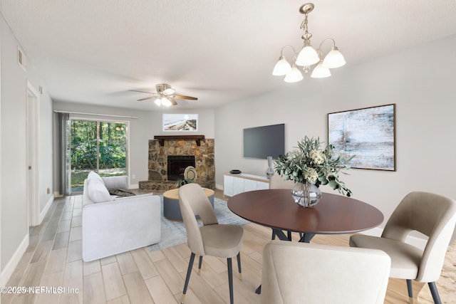 dining space with visible vents, baseboards, wood finish floors, a fireplace, and ceiling fan with notable chandelier