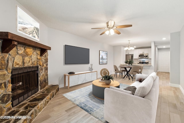 living area with light wood finished floors, baseboards, ceiling fan with notable chandelier, a stone fireplace, and recessed lighting