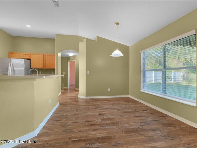 kitchen featuring stainless steel refrigerator with ice dispenser, lofted ceiling, visible vents, a sink, and wood finished floors