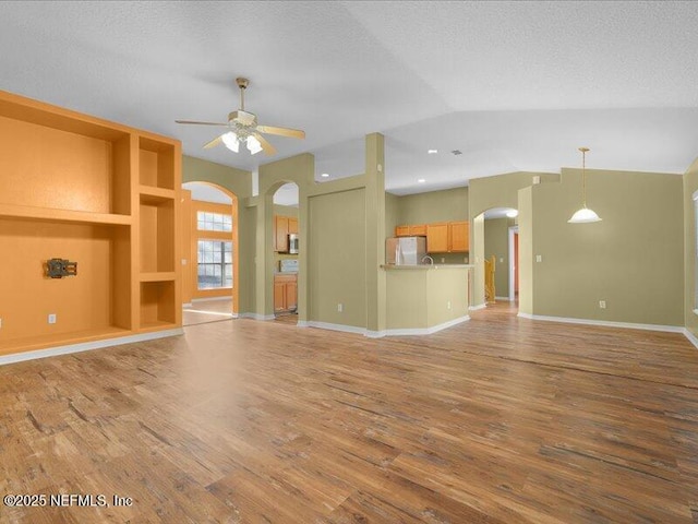 unfurnished living room with arched walkways, ceiling fan, a textured ceiling, and wood finished floors