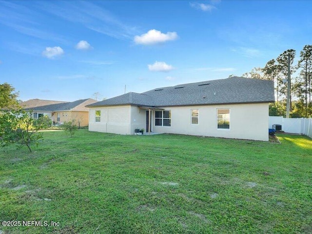 rear view of house with a lawn, fence, and stucco siding