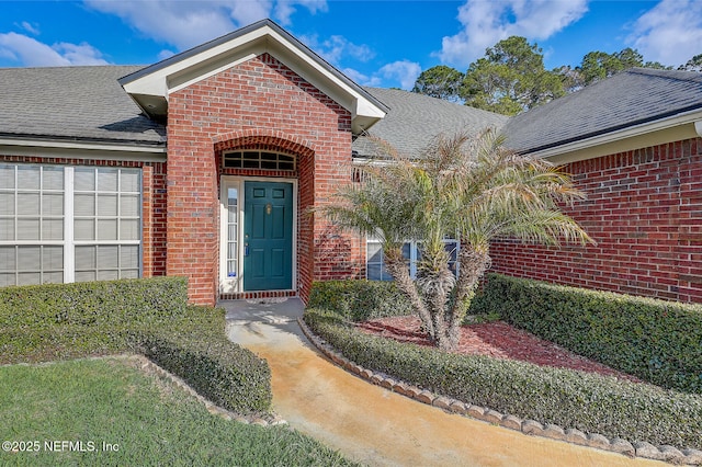 doorway to property with brick siding and roof with shingles