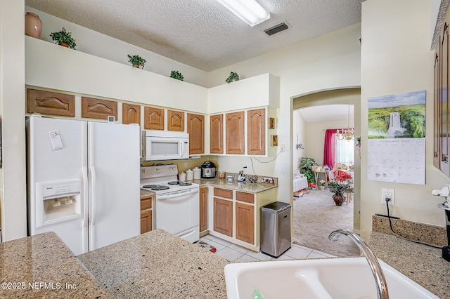 kitchen with arched walkways, a textured ceiling, white appliances, a sink, and visible vents