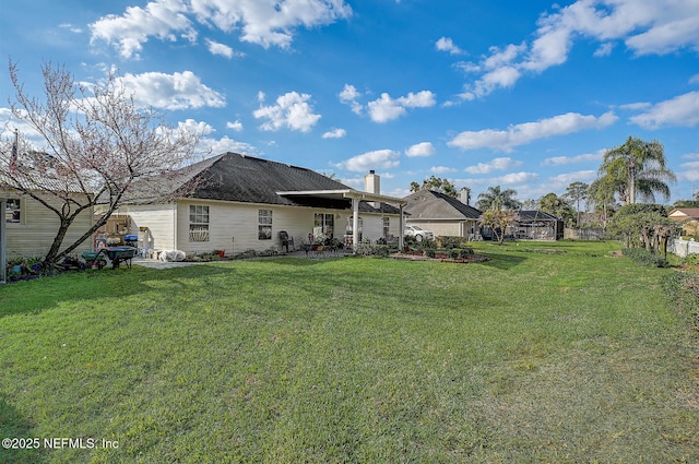 back of house with a chimney, a lawn, and a patio area