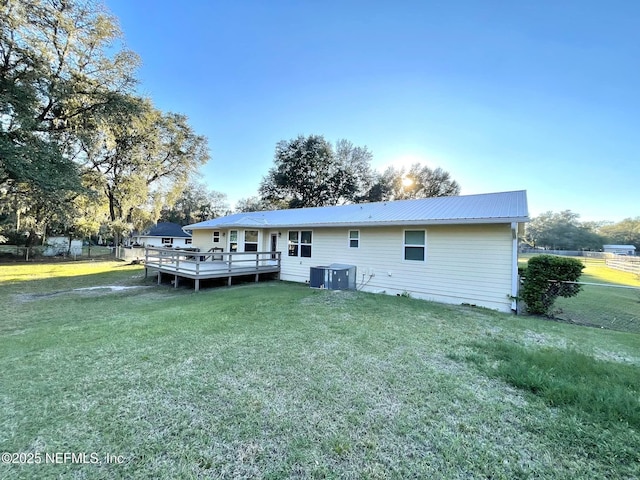 rear view of property with a deck, fence, metal roof, and a lawn