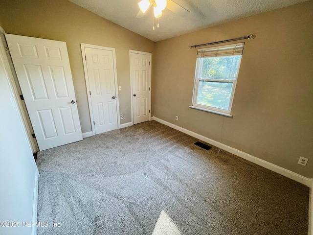 unfurnished bedroom featuring baseboards, visible vents, lofted ceiling, carpet, and two closets