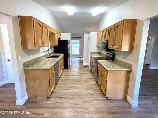 kitchen featuring vaulted ceiling, appliances with stainless steel finishes, a sink, and light wood-style floors