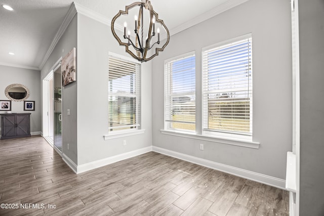 unfurnished dining area featuring baseboards, wood finished floors, a chandelier, and crown molding