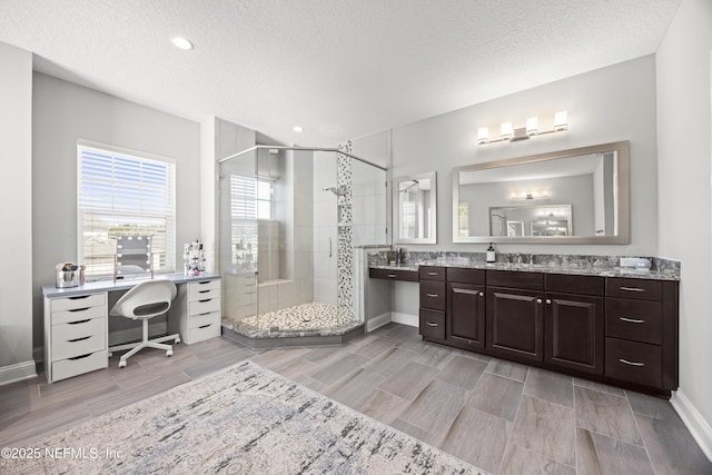 full bathroom featuring vanity, baseboards, wood tiled floor, a shower stall, and a textured ceiling