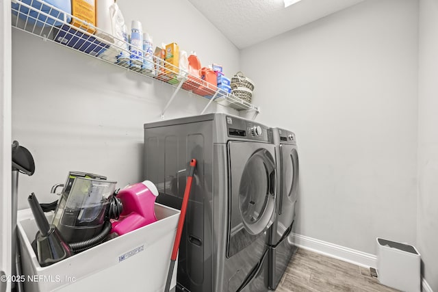 clothes washing area featuring baseboards, laundry area, wood finished floors, independent washer and dryer, and a textured ceiling