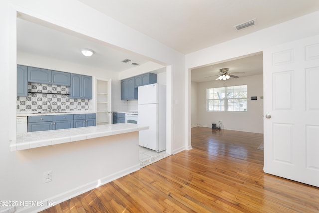 kitchen featuring tile counters, visible vents, freestanding refrigerator, blue cabinets, and light wood-type flooring