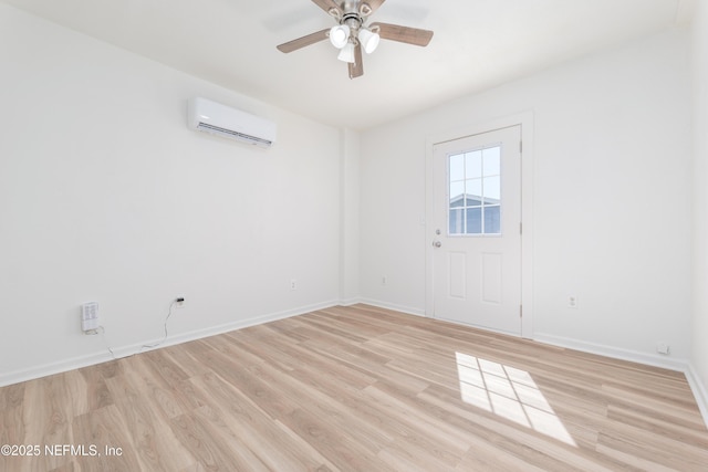 spare room featuring light wood finished floors, ceiling fan, baseboards, and a wall mounted AC